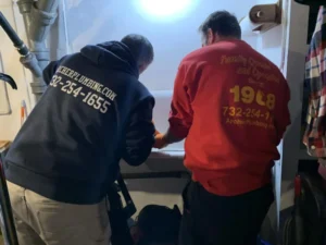 Two plumbers cleaning a drain near a utility sink in Old Bridge, NJ